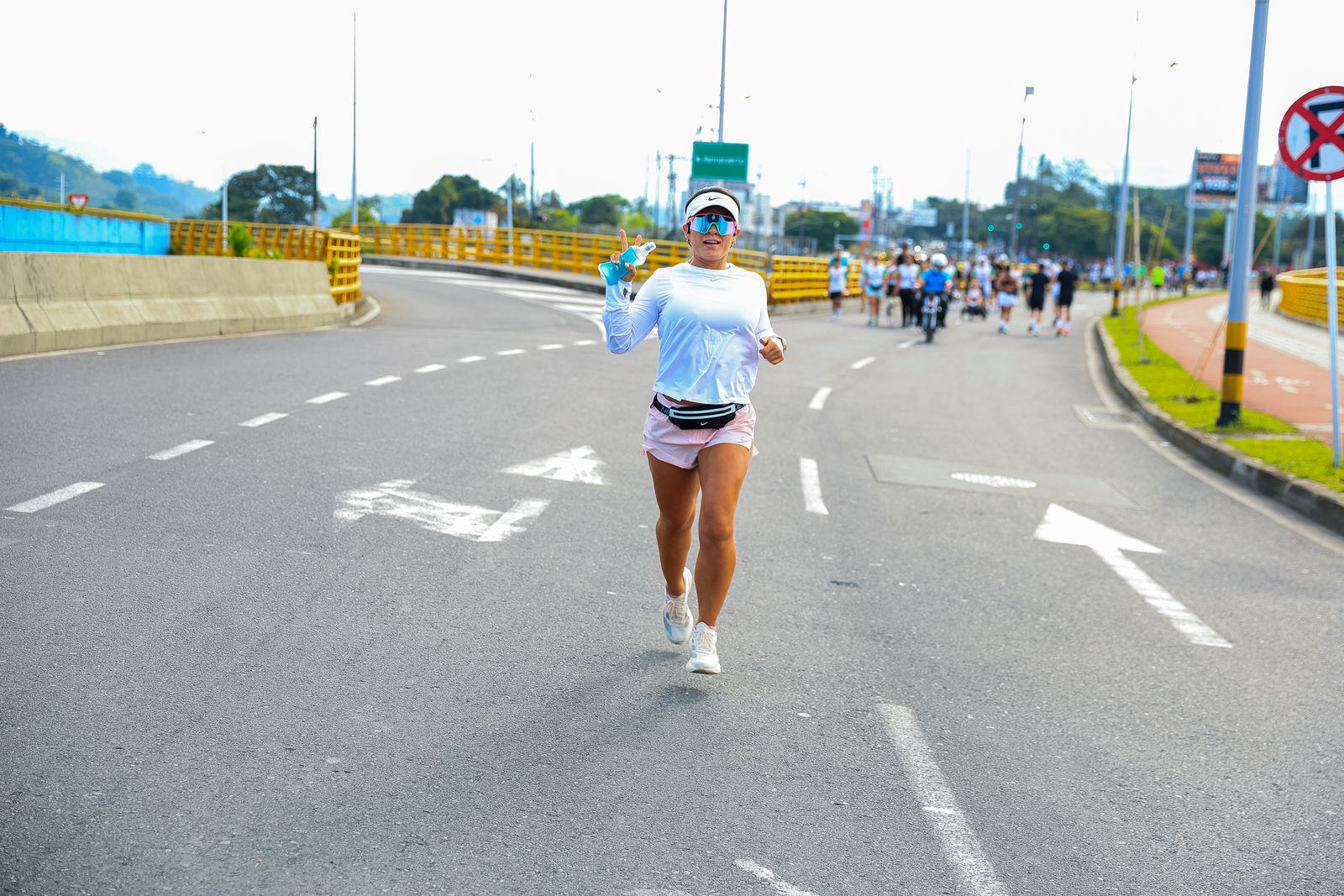 A woman out front of a big road-race field sweeping across a highway bridge